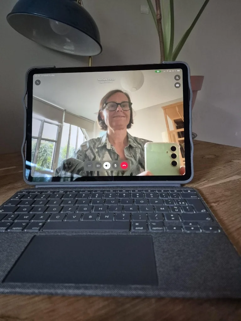 Une tablette affichant une visioconférence avec Nathalie Suzanne sur un bureau en bois
